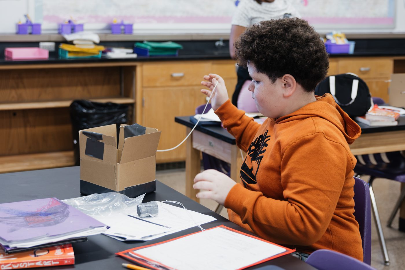 A student threads string through a cardboard box during a build.