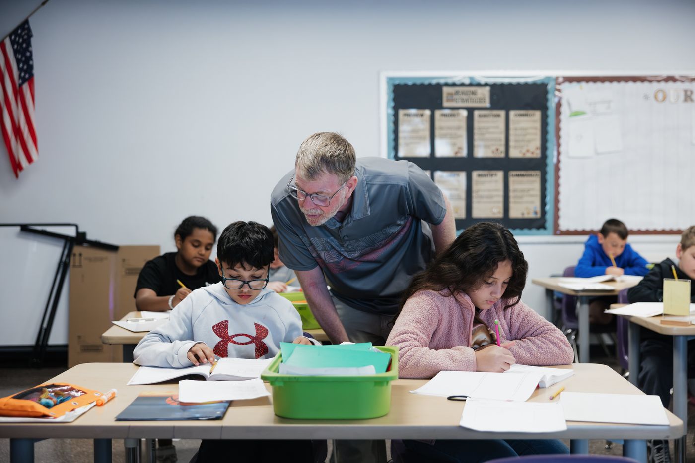 A teacher leans in to help two students with their work.