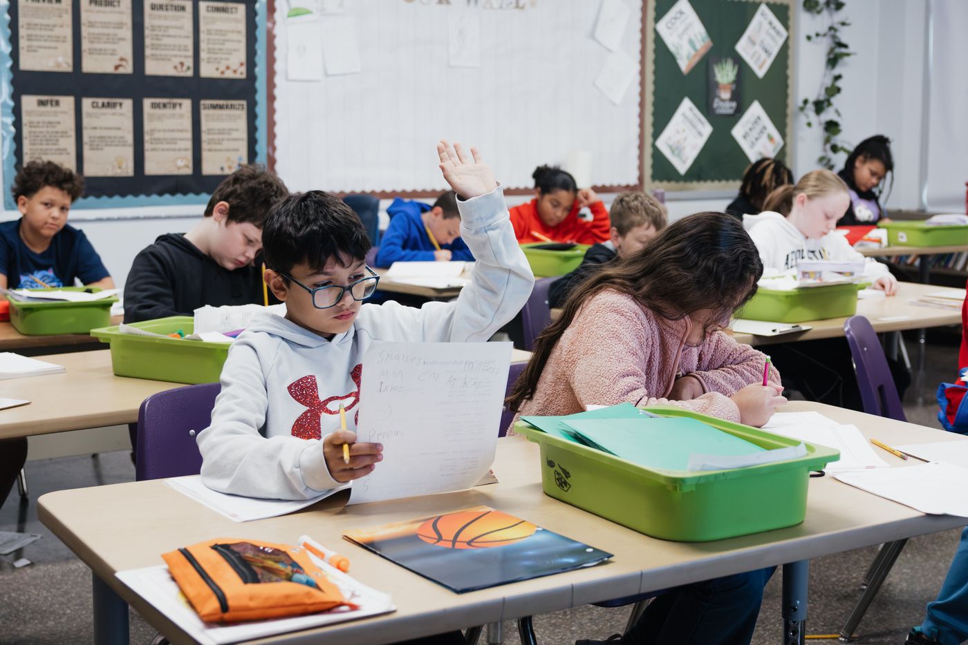 A student raises his hand, holding up his worksheet.