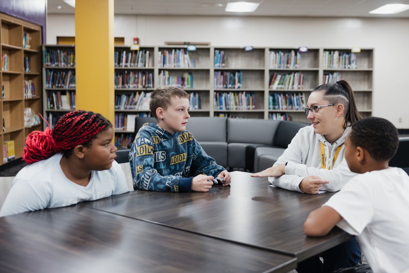 A small group of students talks with a staff member around a library table.