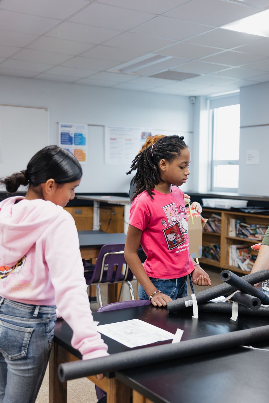 Two students carry foam tubing to their build station.