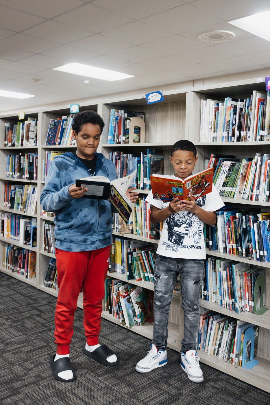 Two students stand in the stacks, reading the books they chose.